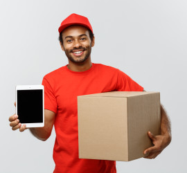 Delivery Concept - Portrait of Handsome African American delivery man or courier with box showing tablet on you to check the order. Isolated on Grey studio Background. Copy Space.